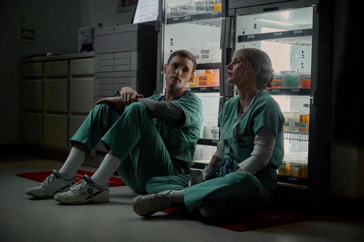 A male and female nurse in scrubs sit on the ground.