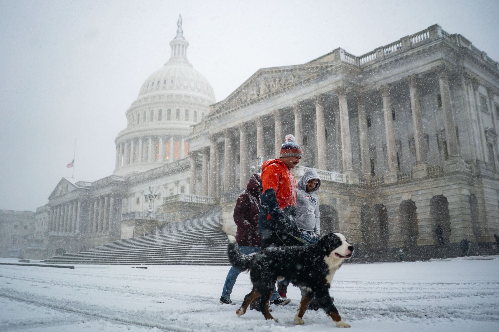 A wide shot of people walking through falling snow in front of U.S. Capitol building