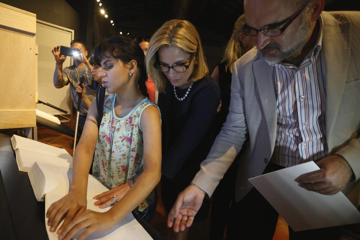 The mayor of San Juan, center, and José Manuel Lucía of the Spanish Royal Academy observe a woman reading the Spanish master work "Don Quixote" in Braille.