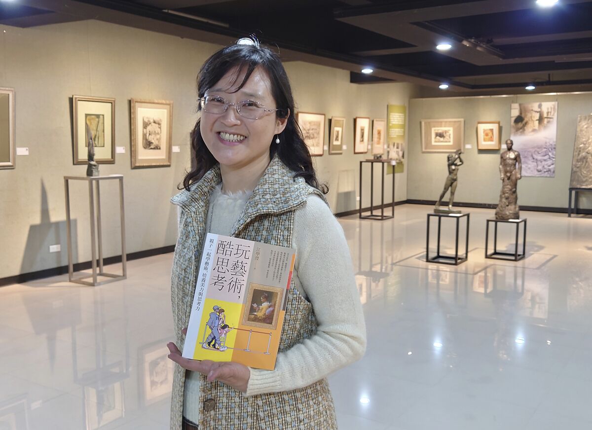 In this photo taken on March 23, 2021, Taiwanese author Iris Chiang holds her book "Play with Art" at the saloon featuring Taiwanese artist YUYU Yang's work in Taipei, Taiwan. Four years on after being sold to a Chinese publisher and no going to press, Chiang's book that teaches children how to appreciate art has fallen victim to the heightened tensions between China and Taiwan that are spilling over into the cultural sphere. (AP Photo/Chiang Ying-ying)