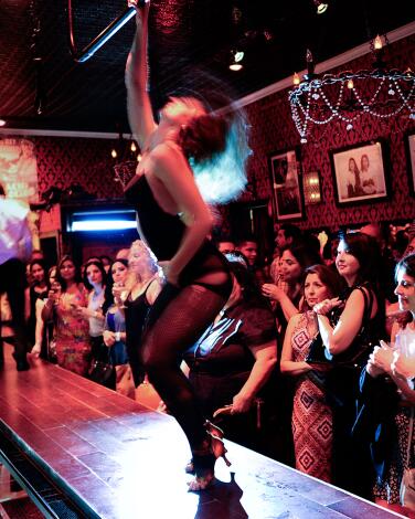 People stand watching a burlesque performance in a bar.