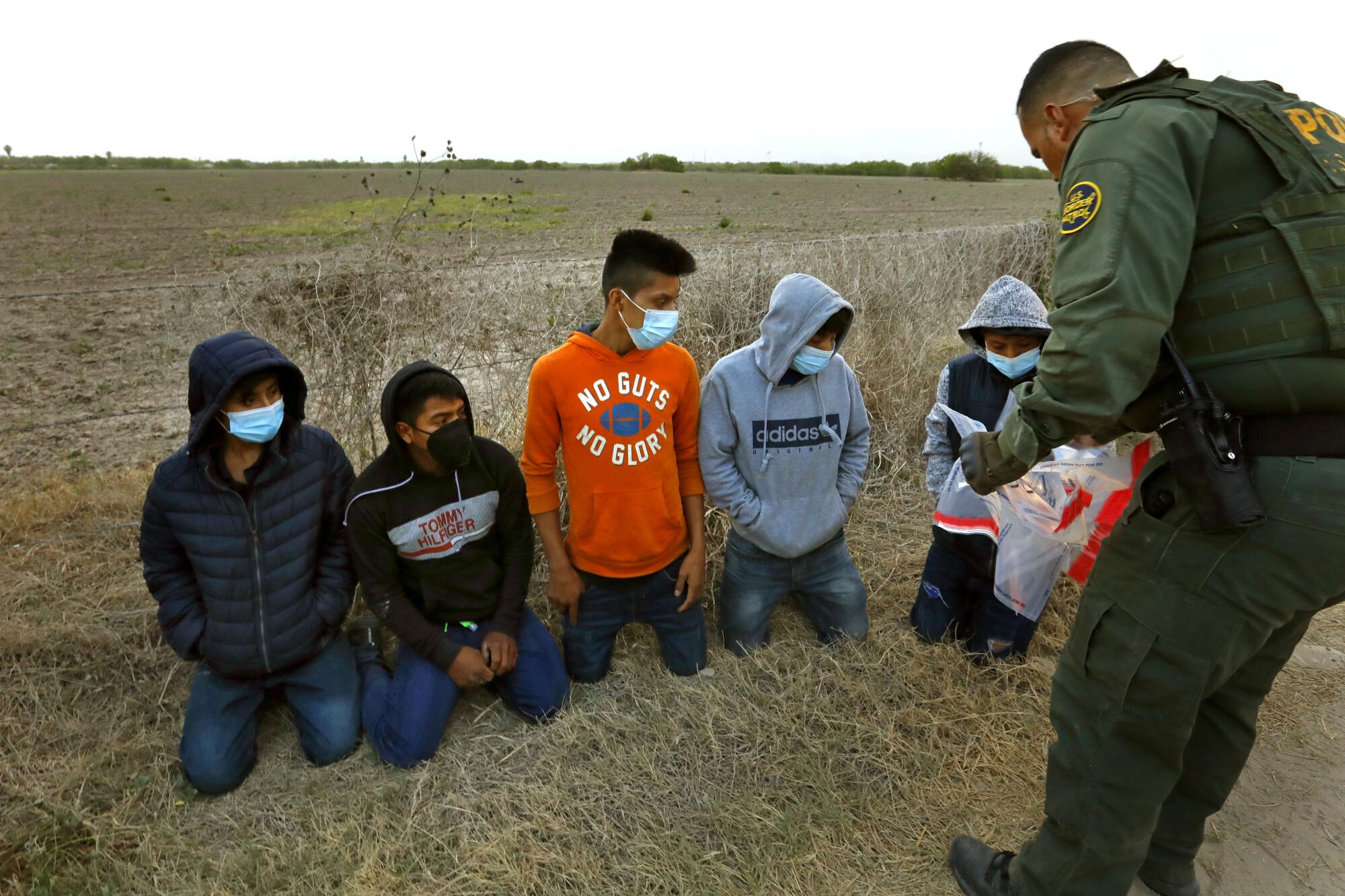 Young migrants on their knees in front of a border agent