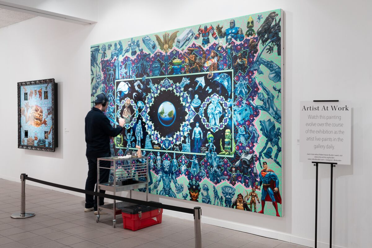 An artist wearing headphones and a backward baseball cap works on a large painting inside a museum.