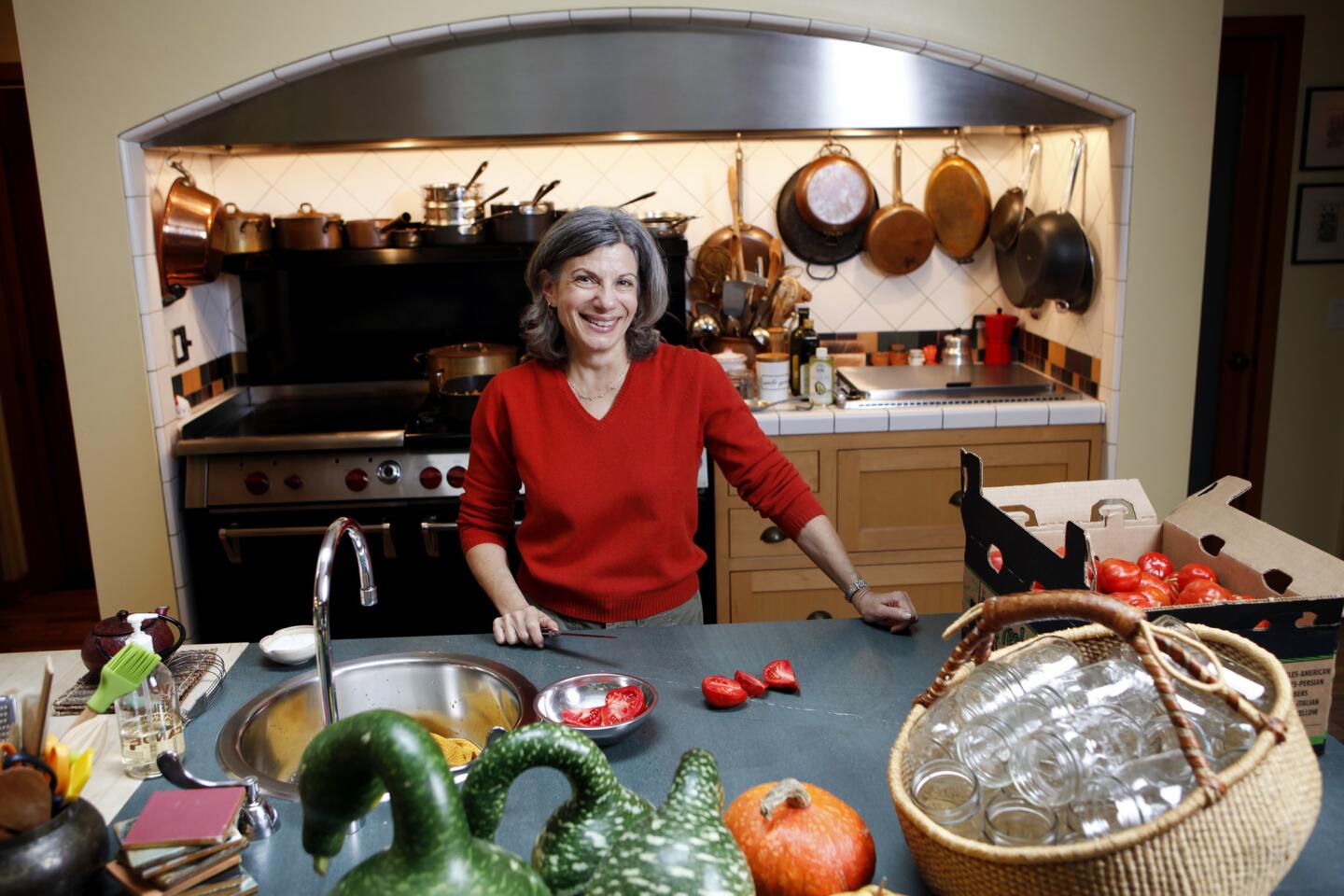 Amelia Saltsman's bounty from a recent farmers market trip includes a case of Costoluto Genovese tomatoes for canning, set atop an island with prep sink. Even when loaded with vegetables, jars and a digital food scale, it doesn't feel crowded. She has drawers instead of cupboards below. In the alcove behind her, where a hood runs the full length, an imposing Wolf Gourmet range has two ovens, six big burners and a big grill. A shelf above holds a luxurious collection of copper and All-Clad pots and pans. There's kosher salt, gray salt, white and black pepper, three olive oils and avocado oil, which Saltsman uses instead of butter for vegan dishes.