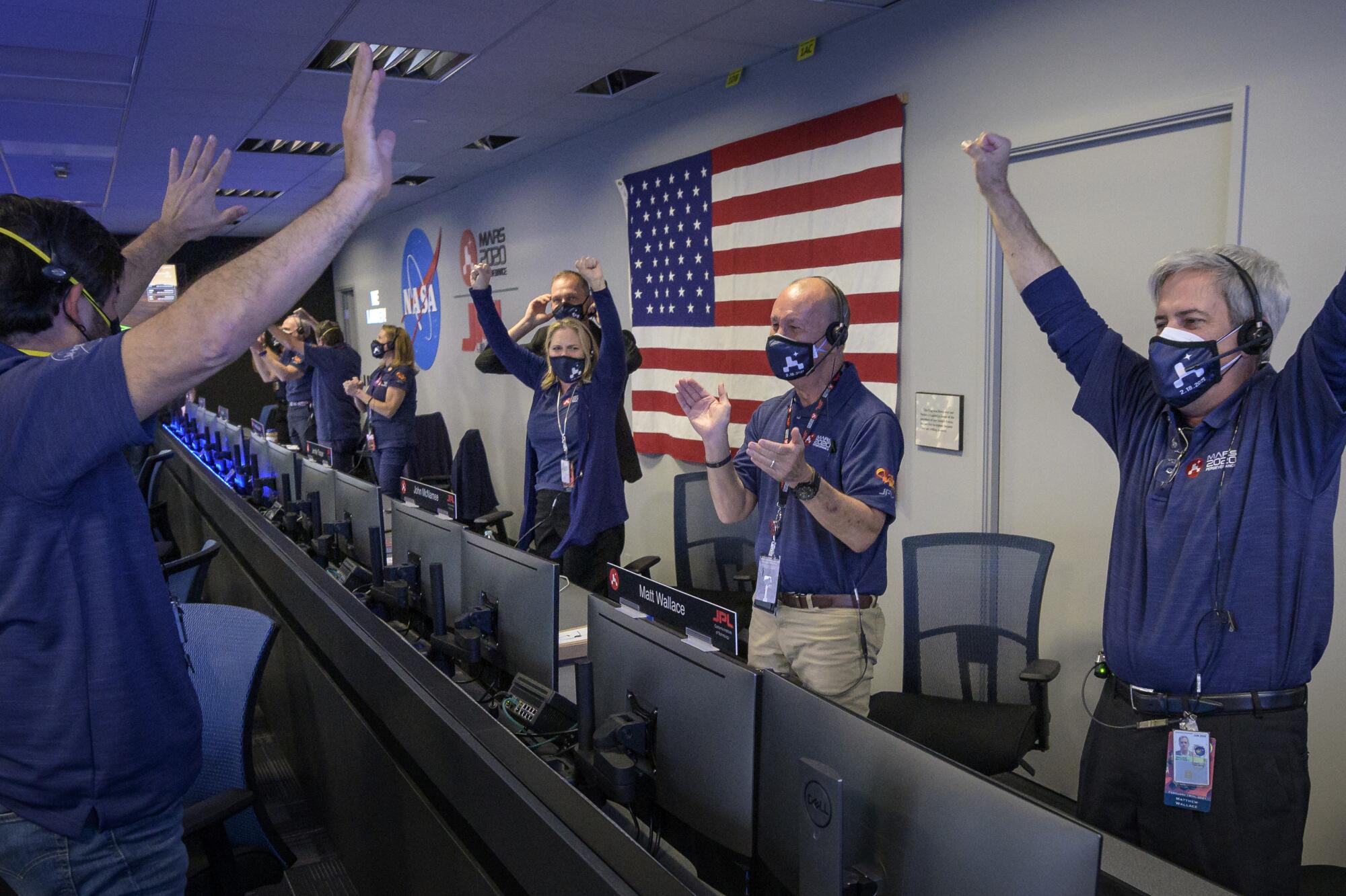 NASA workers raise arms and clap in celebration in mission control