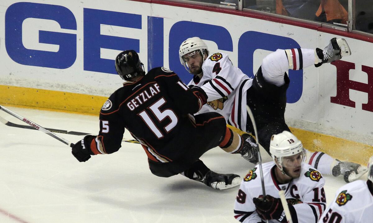 Ducks center Ryan Getzlaf and Blackhawks defenseman Niklas Hjalmarsson slide to the ice as they battle for the puck along the board during Game 7.