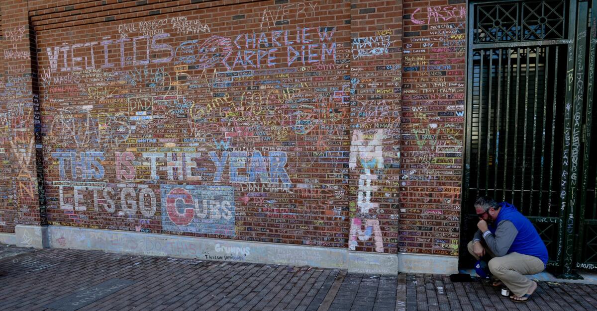 Chicago Cubs fan Britt Sparks holds back tears while kneeling next to the Wrigley Field brick wall in Chicago.