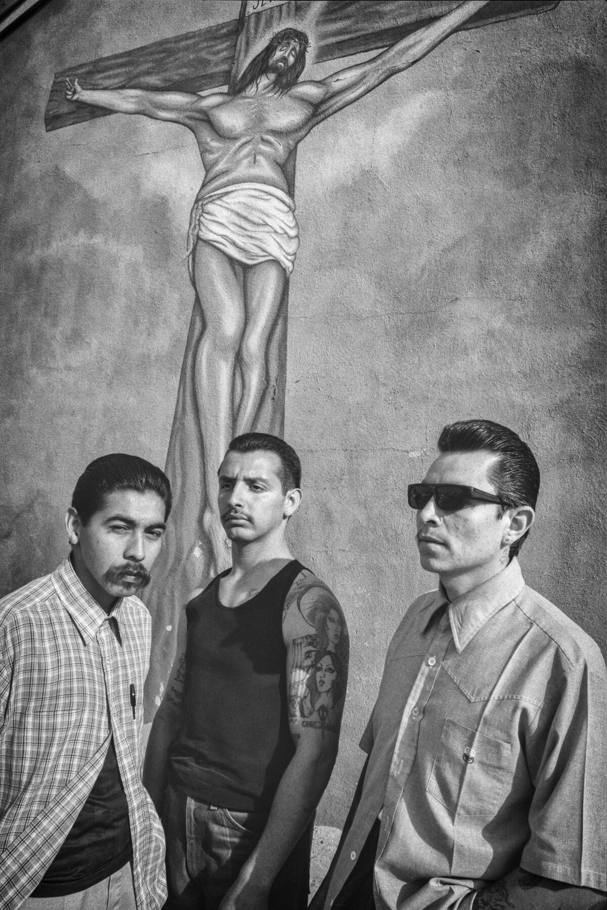 Three young men stand together in front of a mural of the crucifixion of Jesus