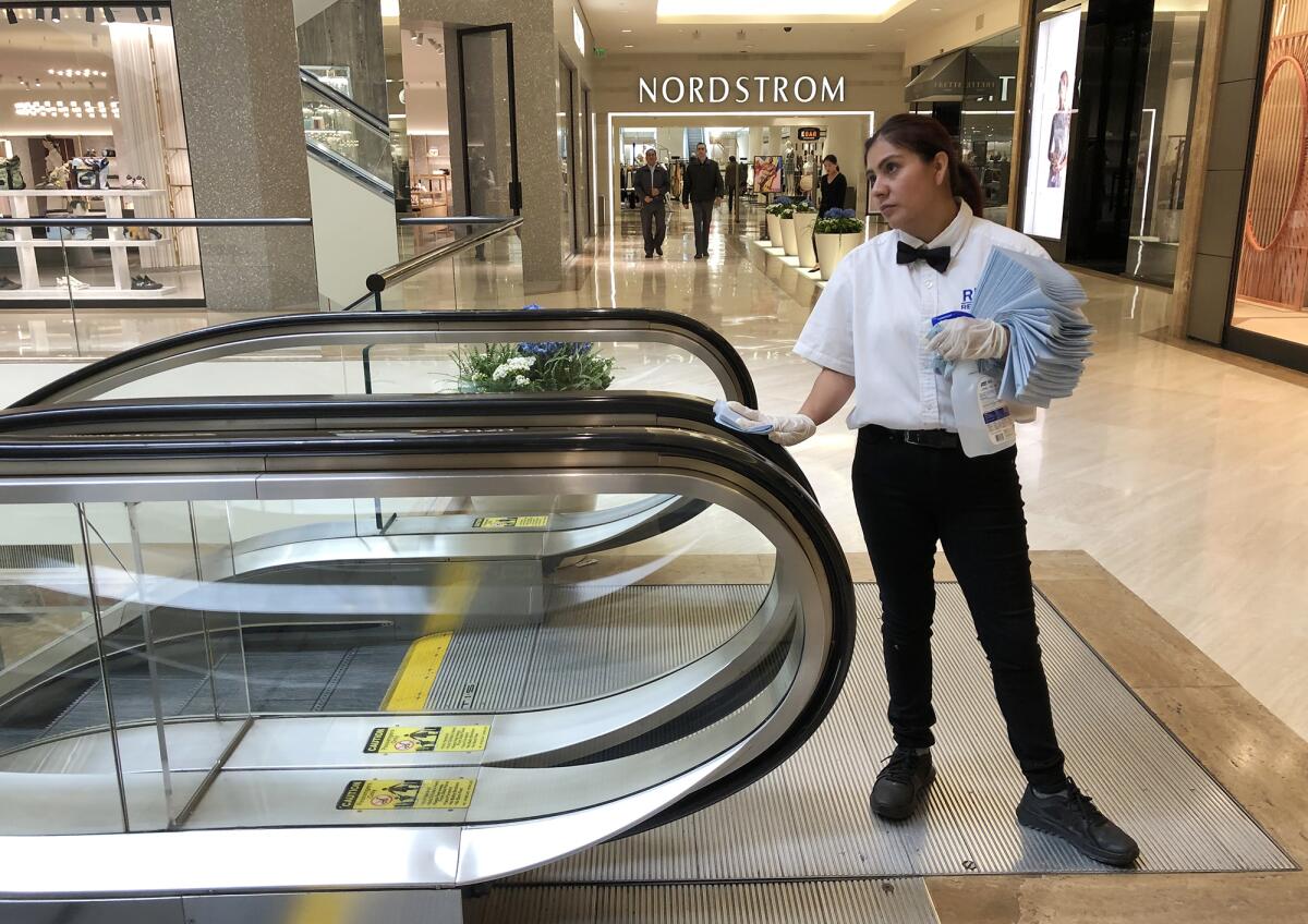 An employee at South Coast Plaza in Costa Mesa disinfects the hand rails of an escalator on March 16. The shopping center closed over a month ago.