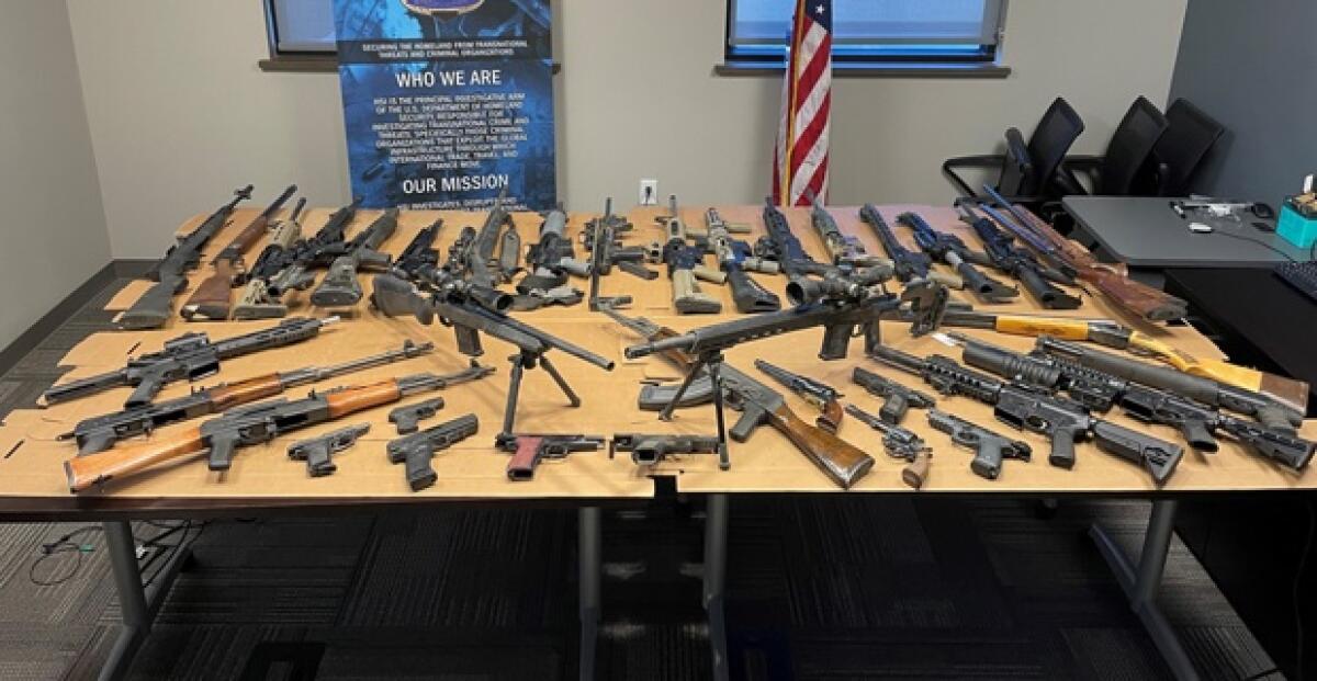 Dozens of firearms are spread out on a table.