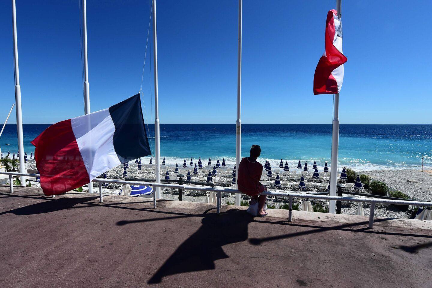 A woman sits under French flags lowered at half-mast in Nice, following the deadly Bastille Day attacks.