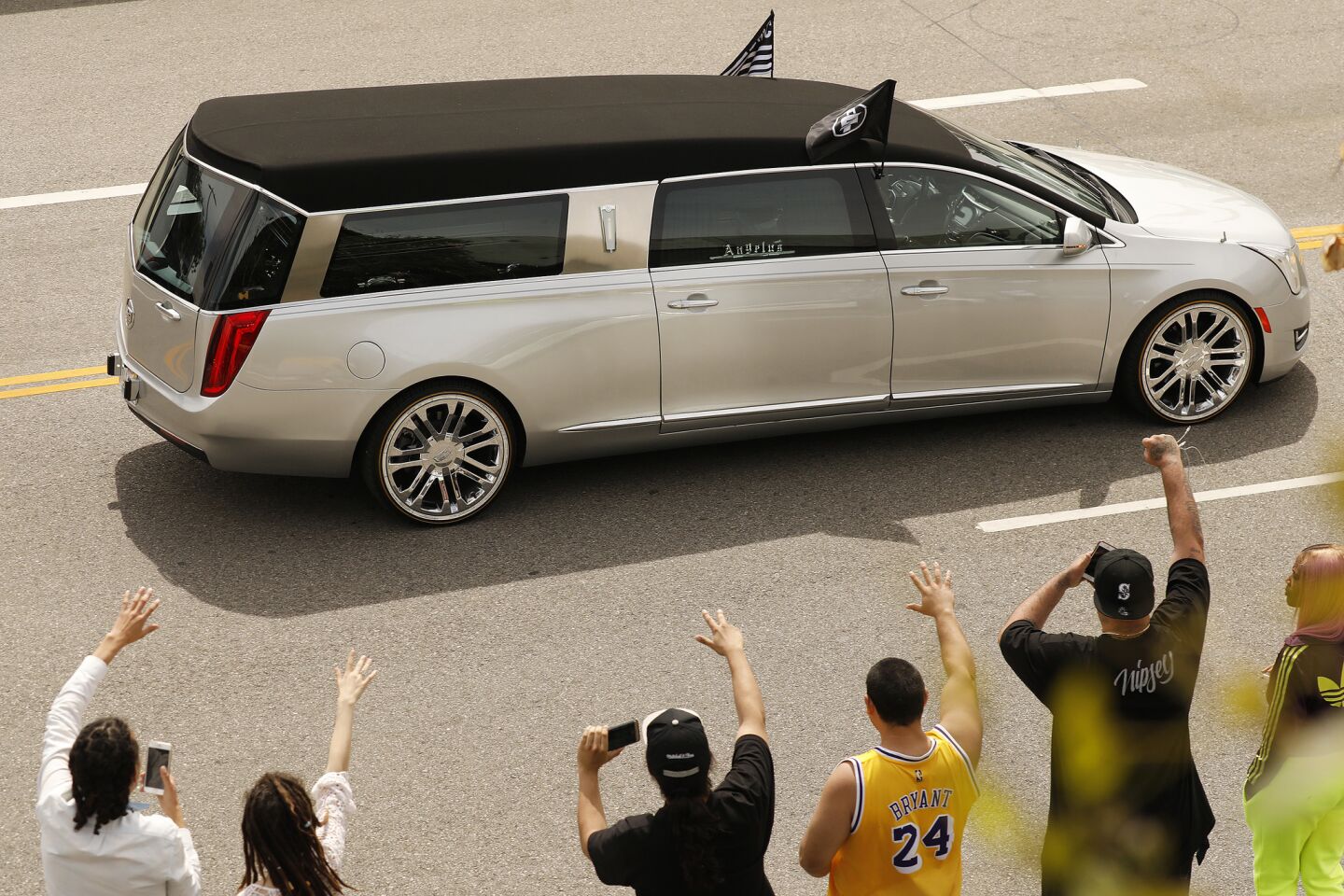 Fans wave as the hearse carrying Nipsey Hussle's body departs Staples Center in a procession after the rapper's memorial.