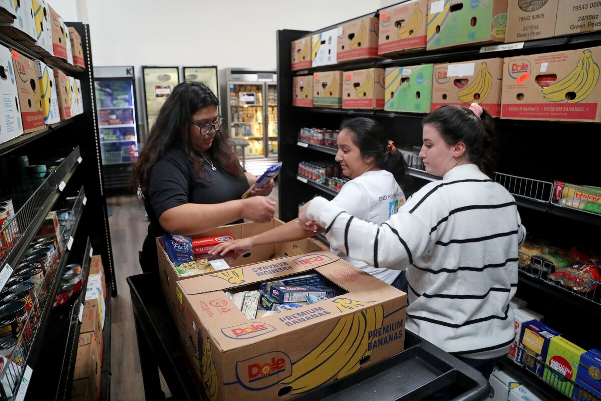 Staffers Chelsea Mascareno, from left, Ruby Osorio and Megan Ryan stock food items at South County Outreach.