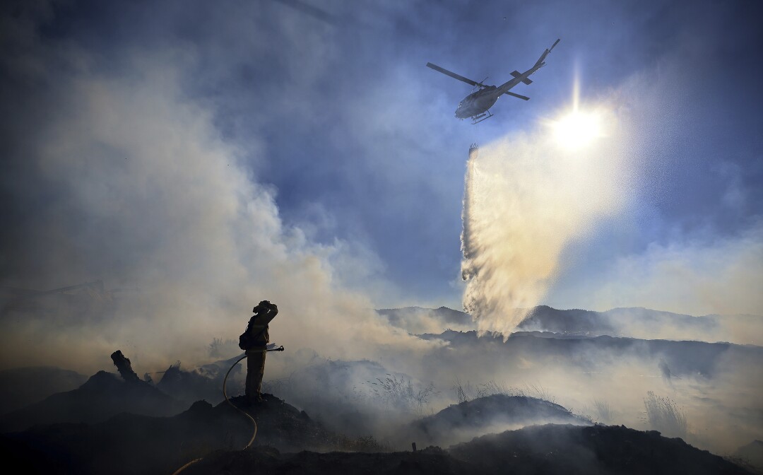 A firefighter stops on a hill as a helicopter flies over