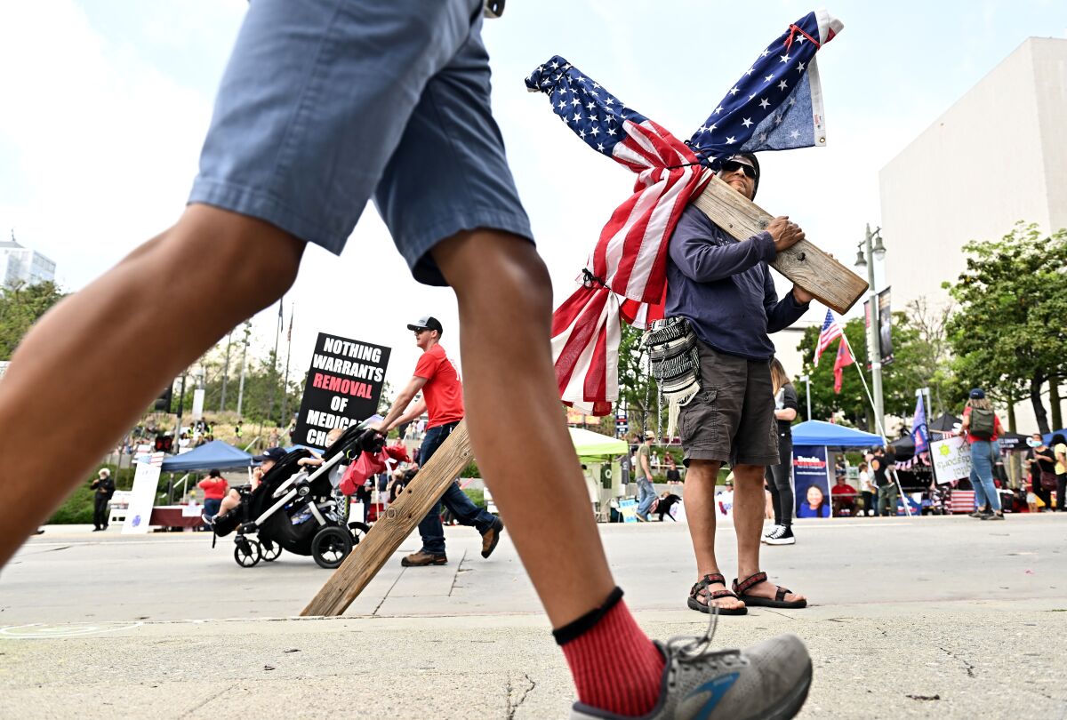 A man holds a cross draped with the American flag during a rally against vaccine mandates.