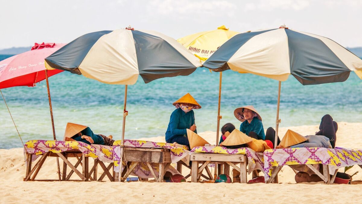 Beach masseuses rest while waiting for tourists in the shade of umbrellas at Long Beach on Phu Quoc Island, Vietnam.