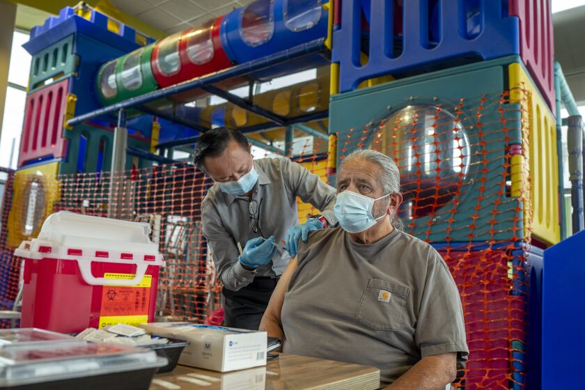FULLERTON, CA - SEPTEMBER 27: Pharmacist Ryan Le, left, gives Jim Canales, 78, of Fullerton a booster shot of Pfizer-BioNTech vaccine at McDonald's on Monday, Sept. 27, 2021 in Fullerton, CA. Canales says his son is a repertory therapist and tells him he must wear his face mask. The Department of Public Health and McDonald's California franchisees continue pop-up vaccine clinics at locations throughout Southern California. They are offering Pfizer, Moderna, and Johnson & Johnson vaccinations and free menu items to the public. (Francine Orr / Los Angeles Times)