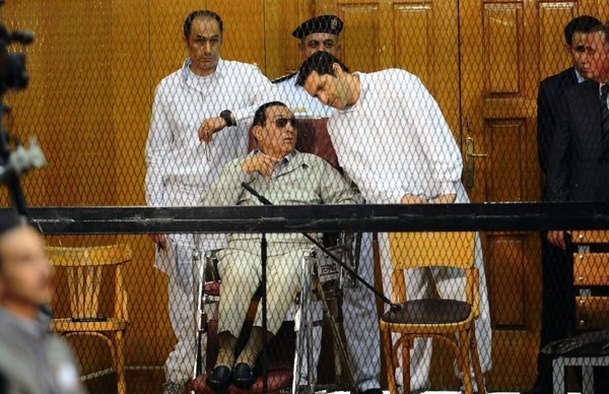 Former Egyptian Pesident Hosni Mubarak and his two sons Alaa, right, and Gamal stand behind bars during their trial in Cairo.