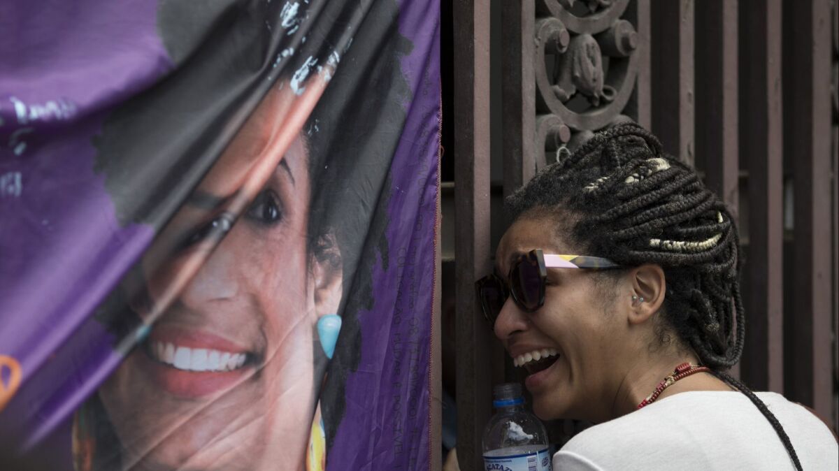 A woman cries next to a banner with an image of Councilwoman Marielle Franco.