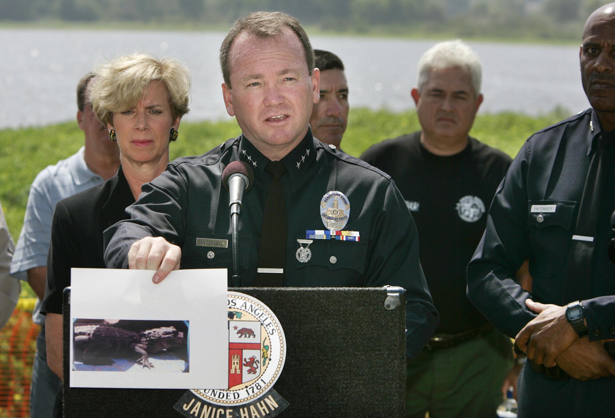 A police officer at a news conference holds up a photo of an alligator 