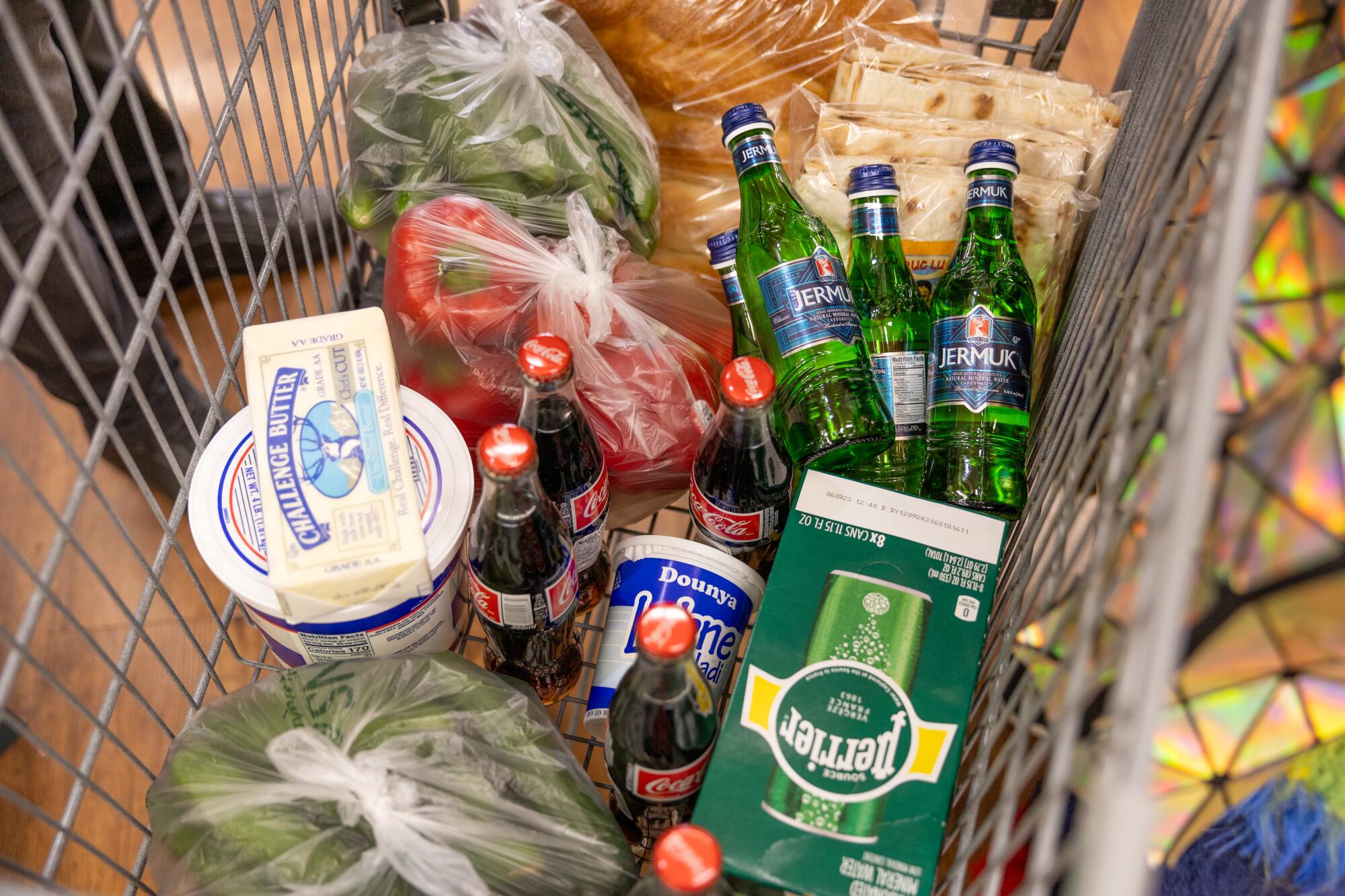 An overhead view of a shopping cart, holding products including butter, veggies and bottles of Coca-Cola and Jermuk water.