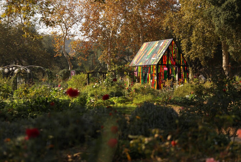 A small colorful building sits amid dense plants and trees.