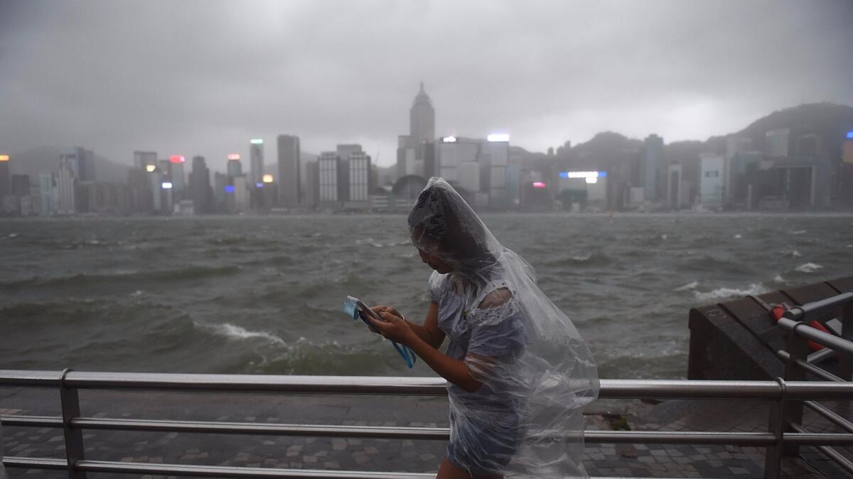 A woman uses her phone while walking near Hong Kong's Victoria Harbor during heavy winds and rain from Typhoon Hato on Aug. 23