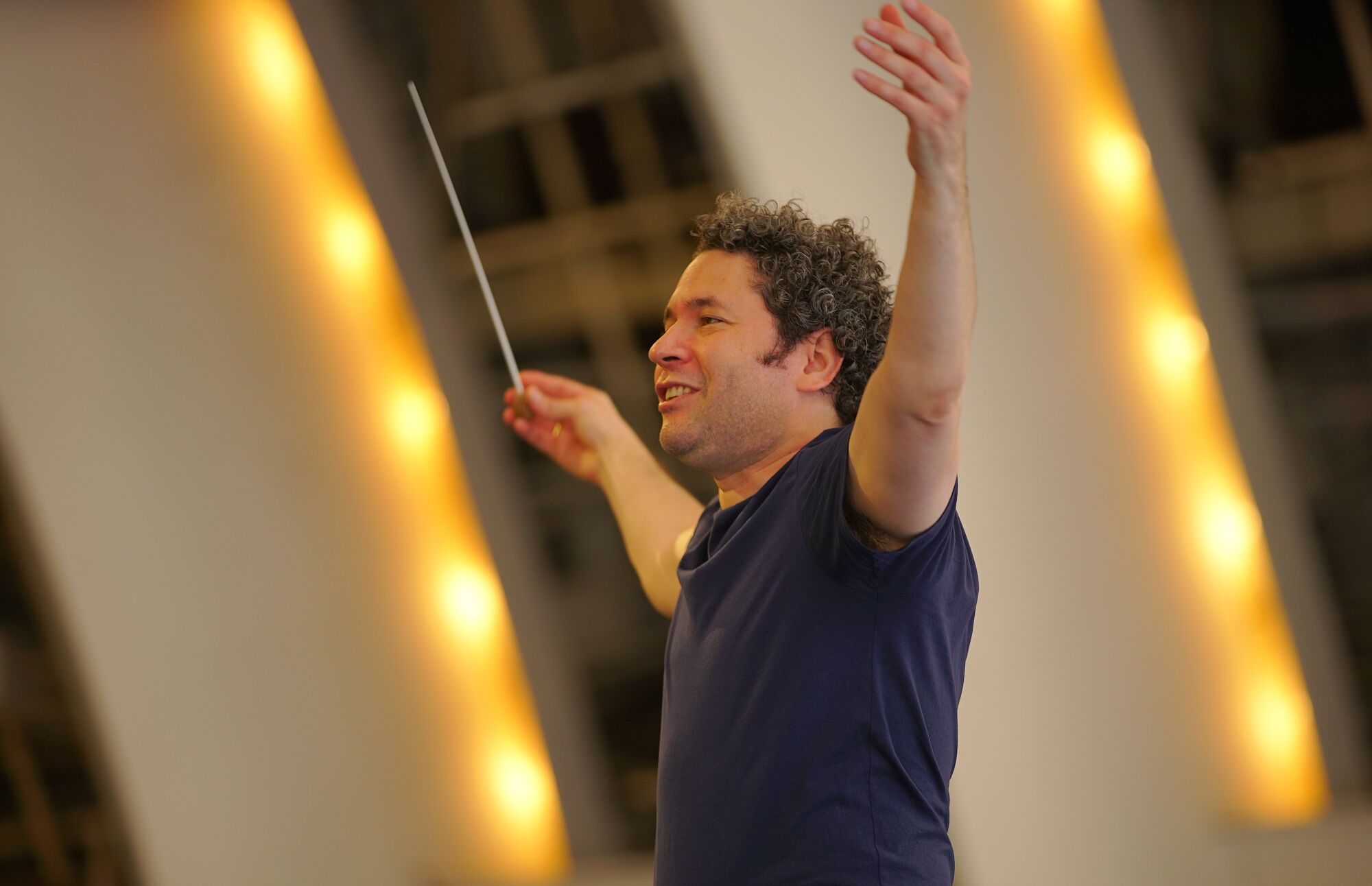 Dudamel, looking exultant, raises his arms with baton in hand