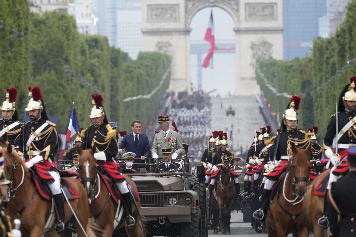 French President Emmanuel Macron, left in car, and French Chief of Staff Gen. Francois Lecointre stand in the command car and review the troops during the Bastille Day parade on the Champs-Elysees avenue, Wednesday, July 14, 2021 in Paris. France is celebrating its national holiday with thousands of troops marching in a Paris parade and traditional parties around the country, after last year's events were scaled back because of virus fears. (AP Photo/Michel Euler, Pool)