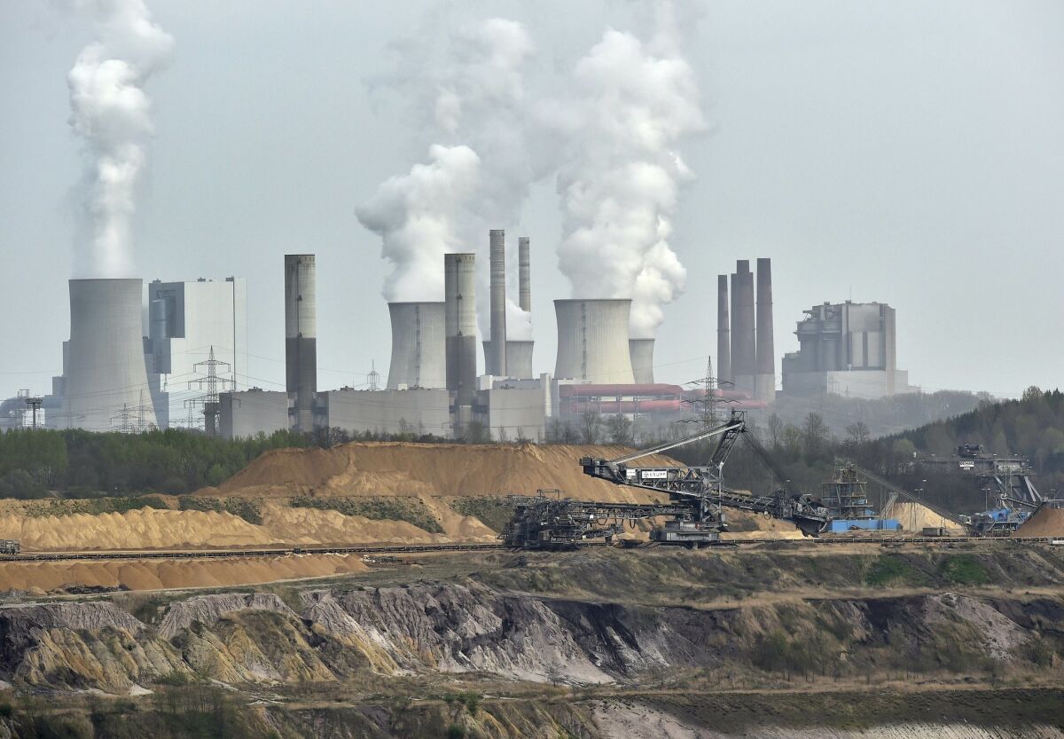 FILE - In this April 3, 2014 file photo giant machines dig for brown coal at the open-cast mining Garzweiler in front of a smoking power plant near the city of Grevenbroich in western Germany.