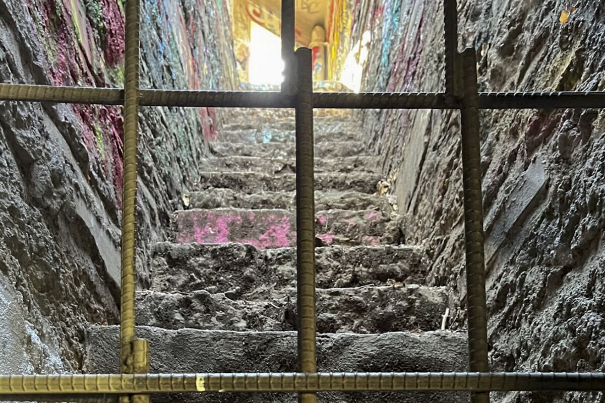 A grid of metal bars in front of a dimly lit, graffiti-covered stairway
