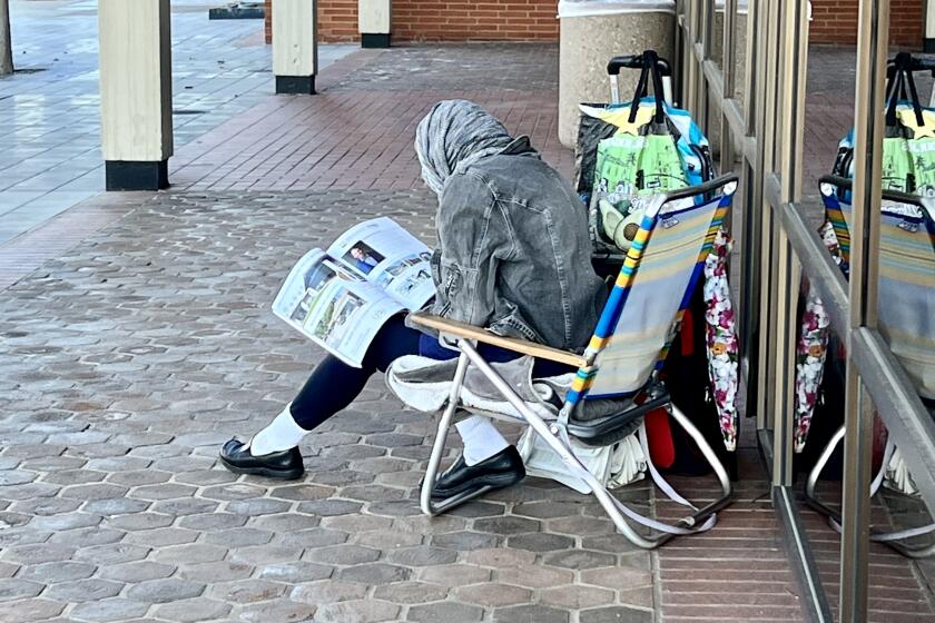 A homeless person reads near her things in La Jolla's Village.