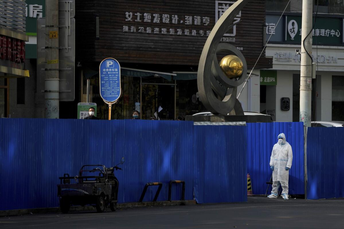 Worker in protective suit near metal screens around shuttered buildings