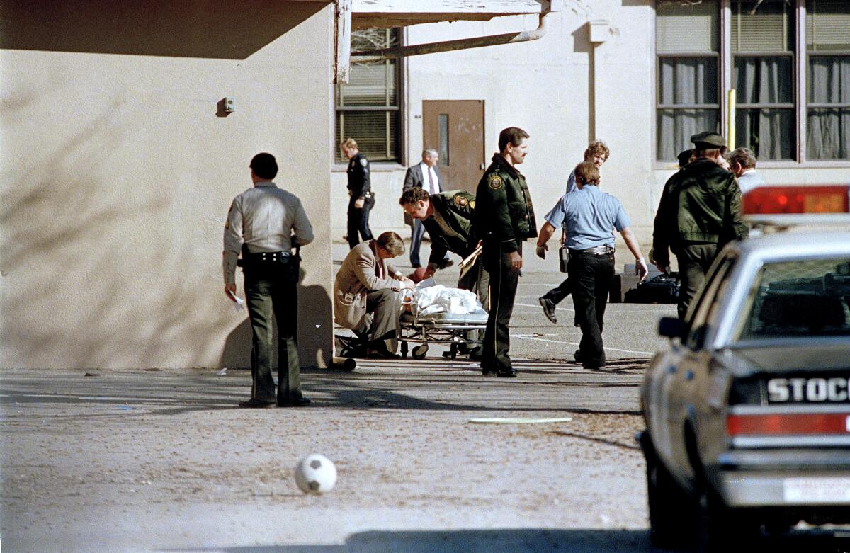 Police around a covered body lying on a gurney in a schoolyard