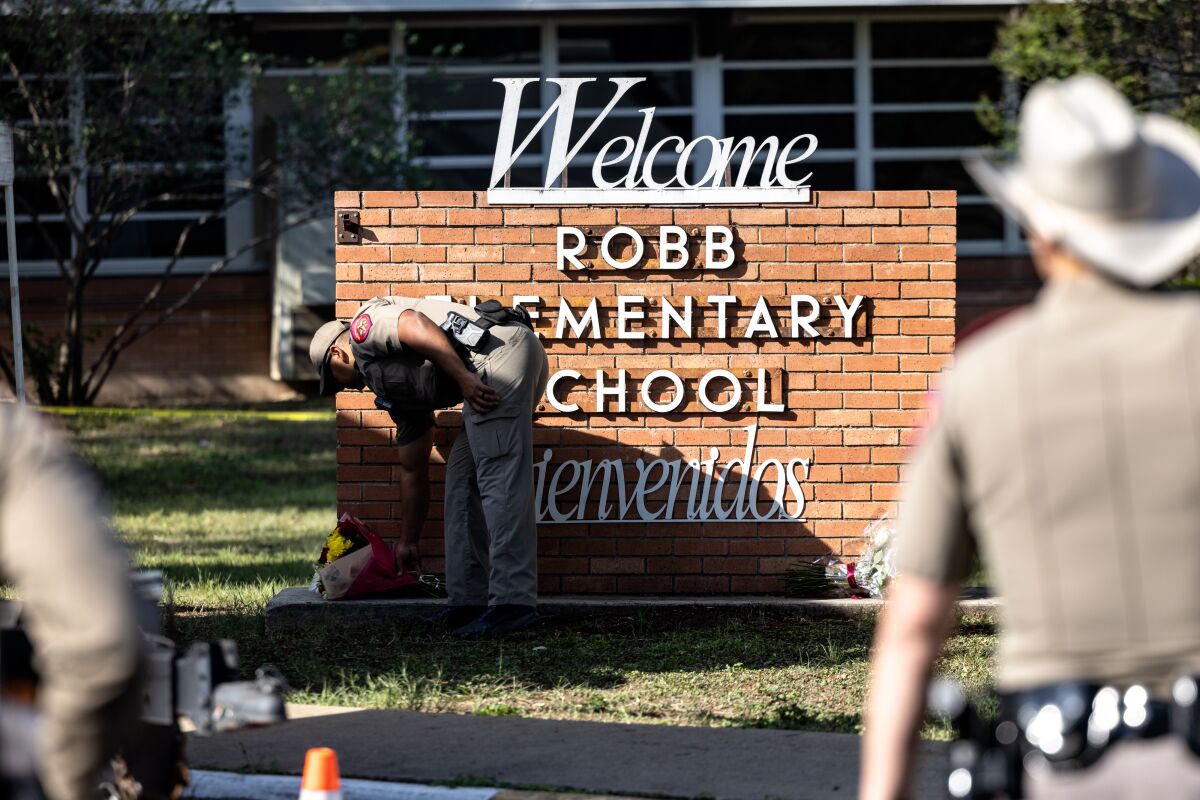 A Texas state trooper places flowers on a sign at the entrance of Robb Elementary School