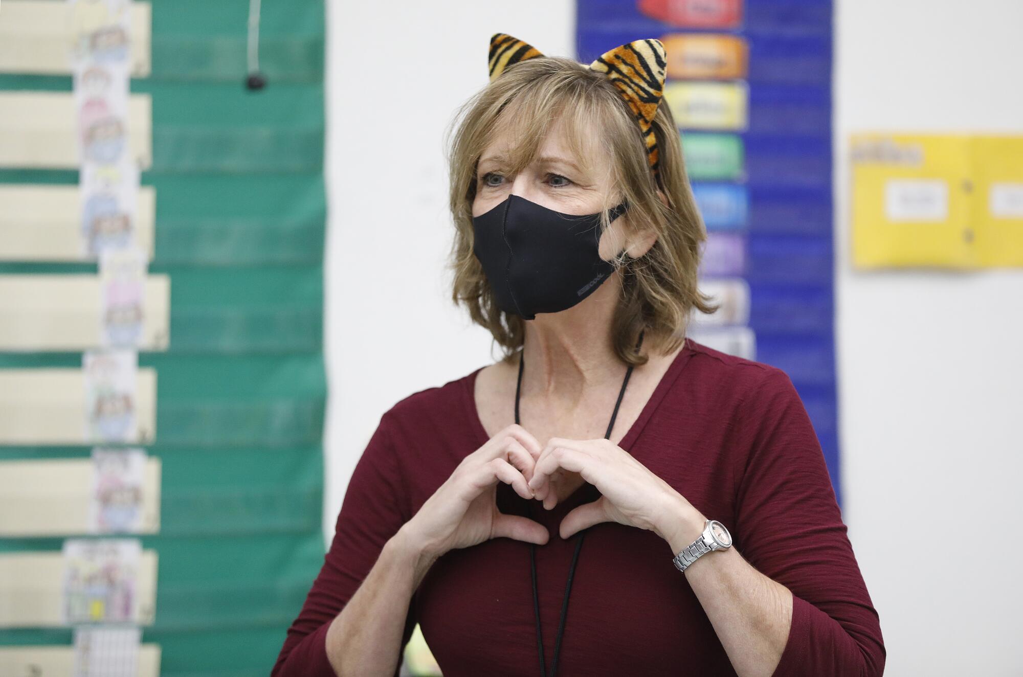 Teacher Jennifer Klein, in mask and cat ears, forms a heart with her hands for students.