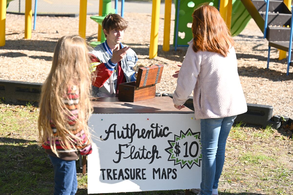 A teenage boy at a stand selling treasure maps to residents of his small town.