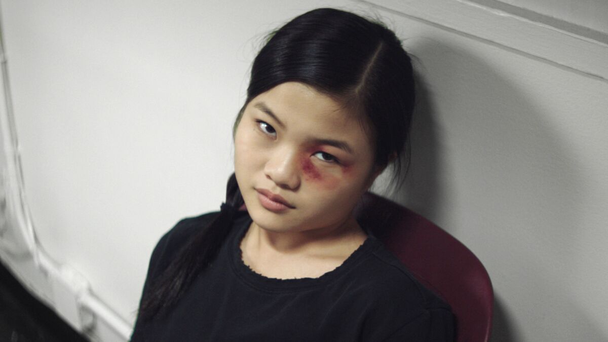 A girl with a bruise under her eye sits on the floor against a wall 
