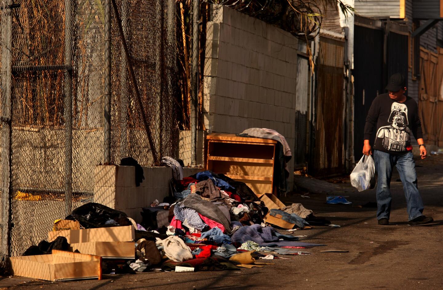 A pedestrian walks past furniture and clothing discarded in an alley in the Pico-Union neighborhood.