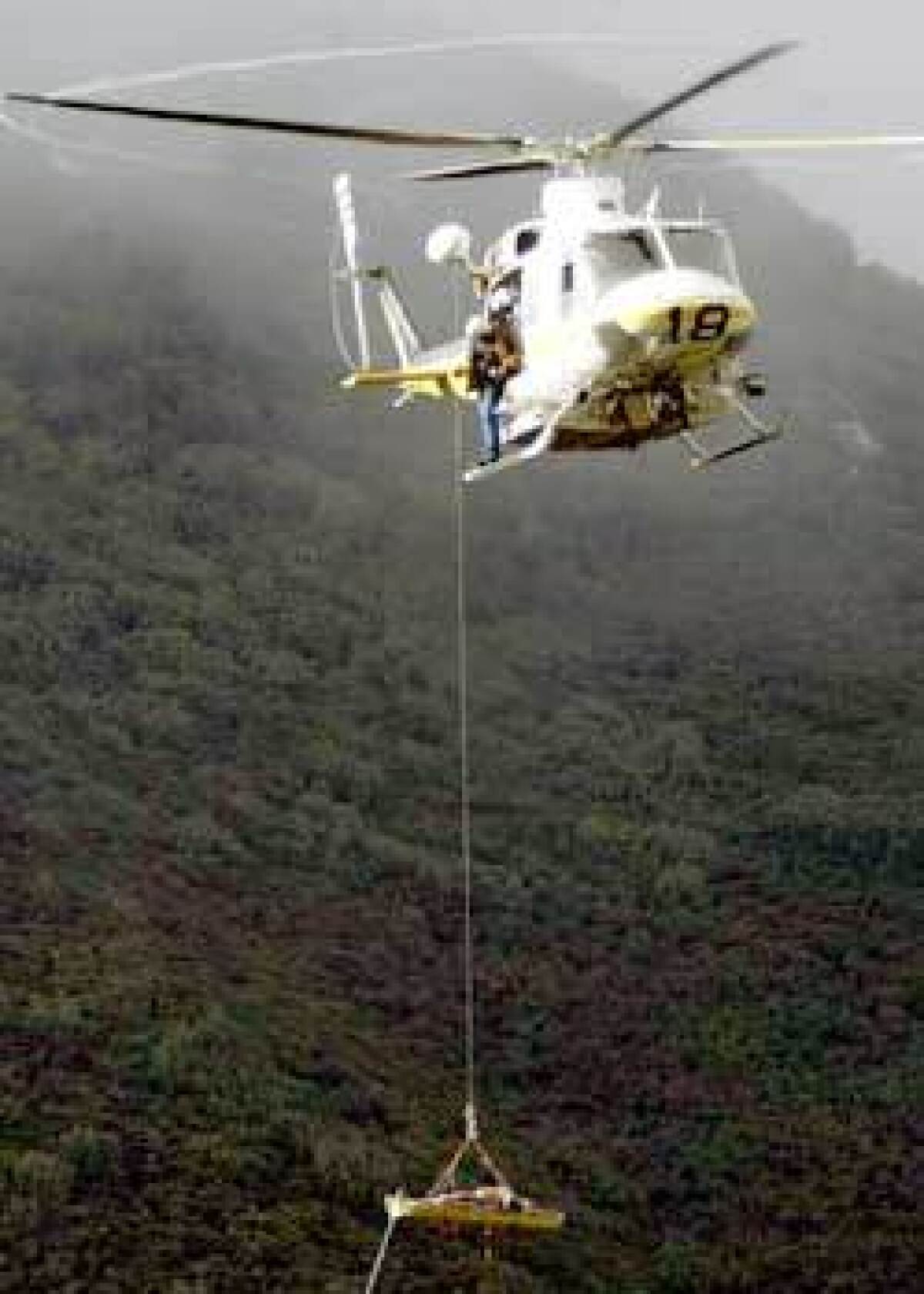 Los Angeles County Fire Department rescue personnel pull a victim out of the ravine where a commuter van carrying workers at NASA's Jet Propulsion Laboratory crashed. The van, on the way to JPL from the Antelope Valley, tumbled about 200 feet down an embankment from the Angeles Crest Highway in the Angeles National Forest. Three workers were killed and two others critically injured.