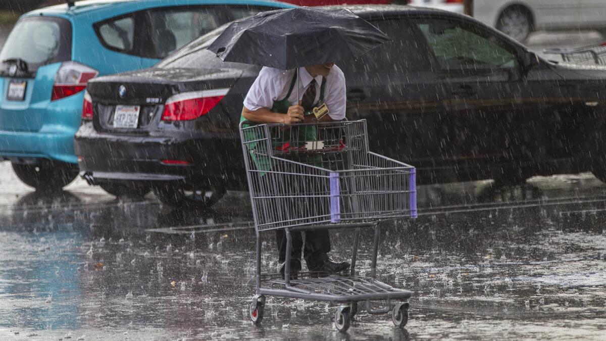 Grocery store clerk Alec Gonzalez keeps his feet dry by riding the cart through pounding rain in Redlands.