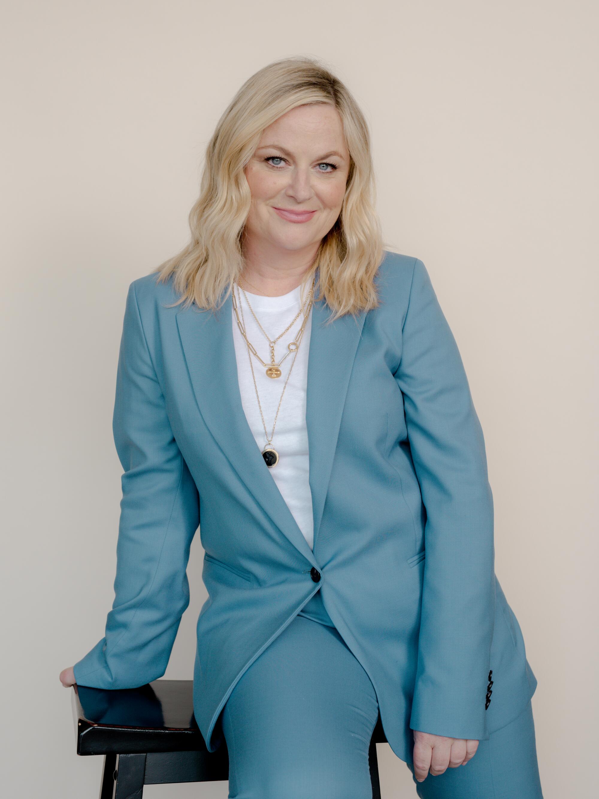 A woman in a light blue suit sits for a portrait against a white background.