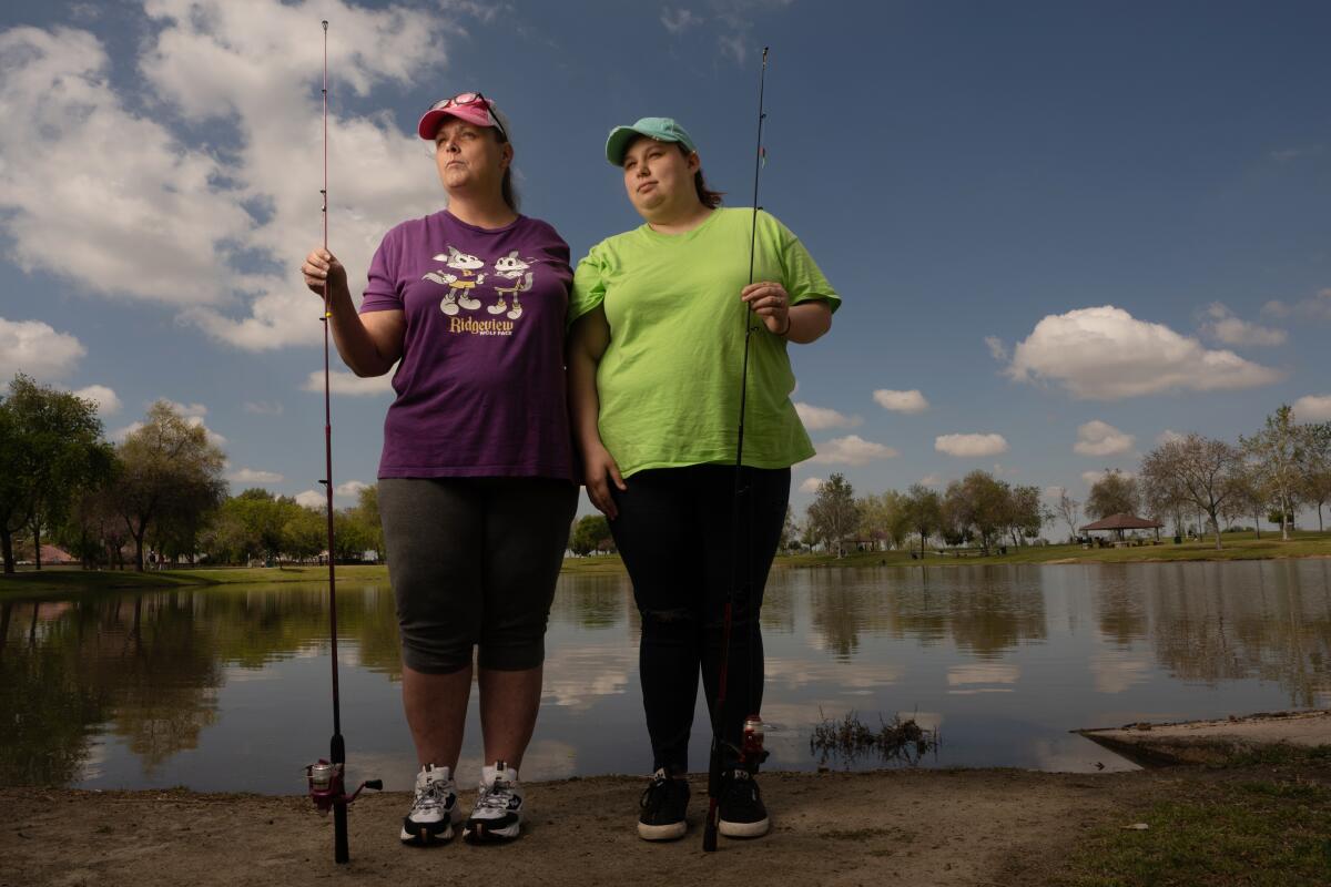 Two women wearing caps and holding fishing poles near the water