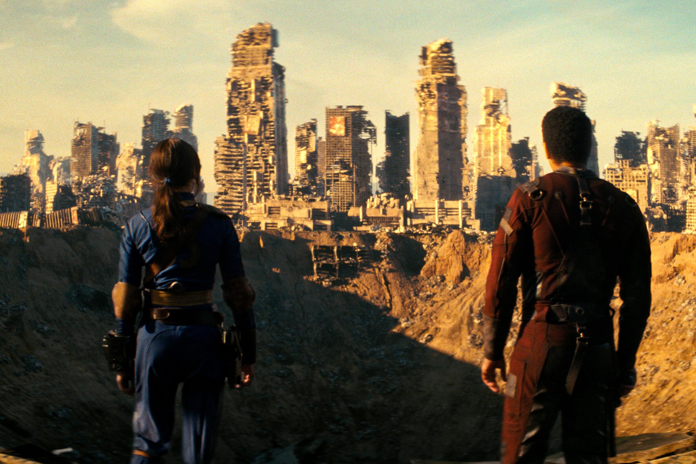 A man and woman look out over a crater with destroyed buildings in the background in "Fallout."