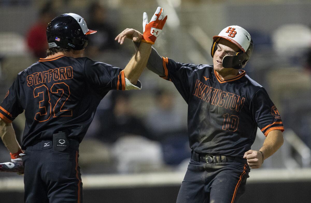 Huntington Beach's Shane Stafford, left, high-fives Noah Madole after he scores on an RBI double from Blake Penso in the fourth inning of the Newport Elks Tournament Frank Lerner Division title game against JSerra at Orange County Great Park in Irvine on Friday.