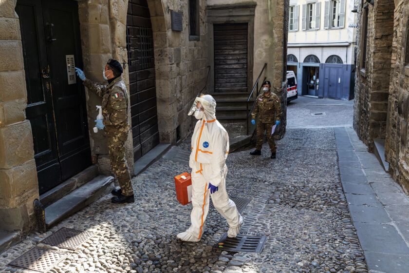 BERGAMO, ITALY - APRIL 6: (EDITORIAL USE ONLY) Two members of the military order of the Italian Red Cross escort in an alley of the old city, a member of the Italian Red Cross during his round of visits to the home of COVID-19 positive patients on April 6, 2020 in Bergamo, Italy. The number of new COVID-19 cases appears to be decreasing in Italy, including in the province of Bergamo, one of its hardest-hit areas. But as the infection rate slows, life is still far from normal. A local newspaper, the Eco di Bergamo, estimates that the province has lost roughly 4,800 people to coronavirus - almost twice an official tally that only counts hospital deaths - and everyone here knows someone who's fallen ill: a neighbor, a family member, a relative, a friend or an acquaintance. The Italian Red Cross, which runs an ambulance service here, continues to field constant calls for help. With only a small portion of its 600-person volunteer crew and 38 paid staff able to report for duty, those who remain work shifts of up to 20 hours long. (Photo by Marco Di Lauro/Getty Images)