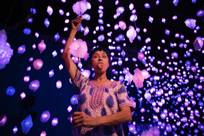 ipilotti Rist sticks out her tongue while standing amid dozens of pink and purple lights that dangle from the ceiling.