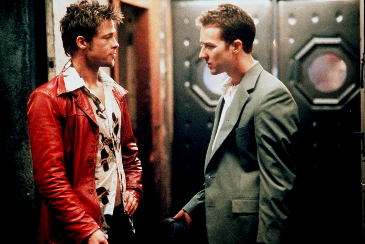 In a scene from 'Fight Club,' Brad Pitt in a red leather jacket talks in a hallway to Edward Norton, who wears a gray suit