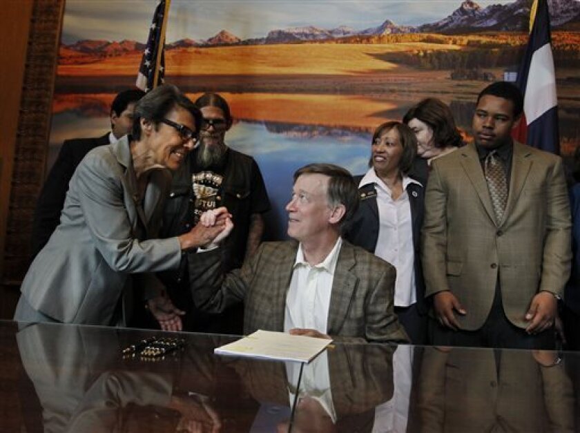 Colorado Gov. John Hickenlooper, center, shakes hands with state Sen. Lucia Guzman after signing a bill she helped sponsor that compensates those wrongly convicted for their time behind bars.