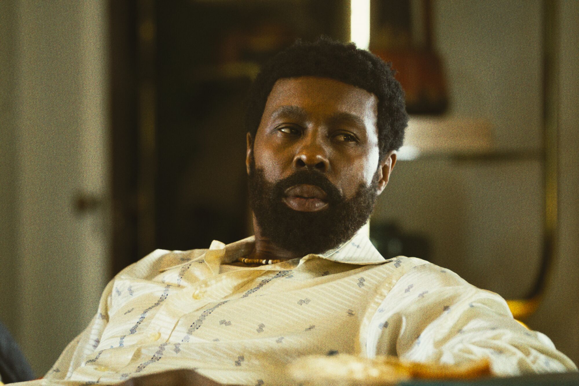A man in a yellow patterned shirt leans back in a chair